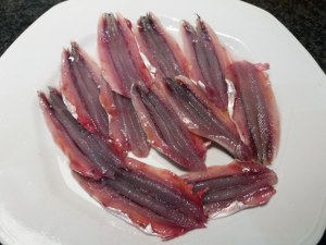 Alici marinate all'arancia su scarole con olive nere capperi pinoli e uva passa